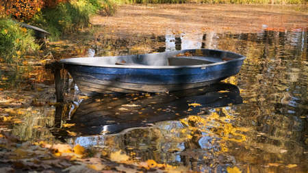 Old wooden boat moored to shore of pond surrounded by lots of colorful autumn leavesの写真素材