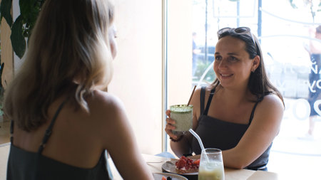 Young caucasian female friends talking and drinking coffee at table in cafeの写真素材