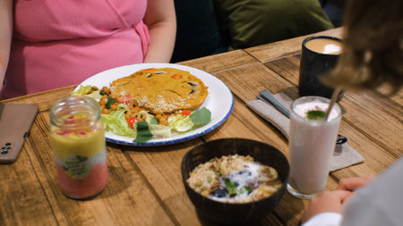 Mom with daughter eating in vegan restaurant, chickpea omelet with mushrooms and raff coffee. Healthy organic vegetarian breakfast conceptの写真素材