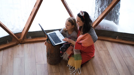 Young woman with little daughter using laptop on Christmas day, typing greetings to friends or relatives on a laptop on the floor of dome campingの写真素材