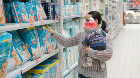 Young caucasian woman with baby in hands choosing diapers at store. NOVOSIBIRSK, RUSSIA, NOVEMBER 21, 2022のeditorial素材