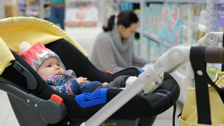 Cute baby resting in stroller while mother buying diapers at store, selective focusの写真素材
