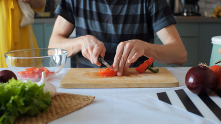 Man cutting red bell pepper for vegan salad while his wife carrying baby over himの写真素材