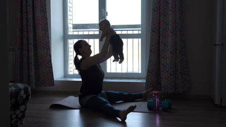 Silhouette of young woman lifting up her baby while working out at homeの写真素材