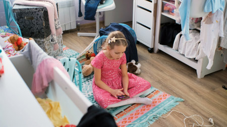 Little girl playing online game while sitting on the floor in her messy roomの写真素材