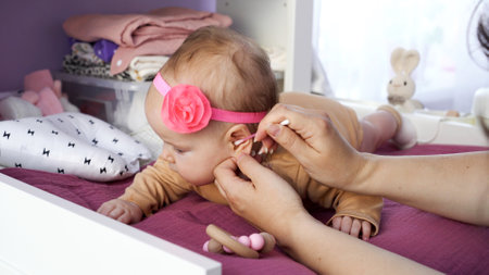 Young mother cleaning baby ear with cotton swab on changing table. Hygiene of infant conceptの写真素材
