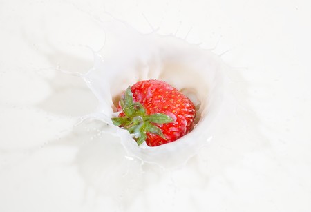 A fresh red strawberry splashing into milkの写真素材