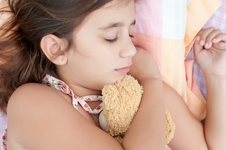 Latin girl sleeping in her bed and hugging a stuffed teddy bearの写真素材