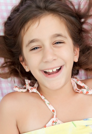 Beautiful hispanic girl laughing in her bed with a pink plaid sheets backgroundの写真素材