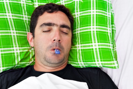 Portrait of a sick hispanic man laying in bed with a thermometer in his mouth and his eyes closedの写真素材