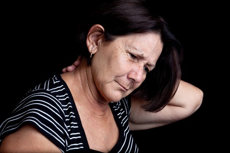Mature woman suffering from neck or shoulder pain on a black background with space for textの写真素材