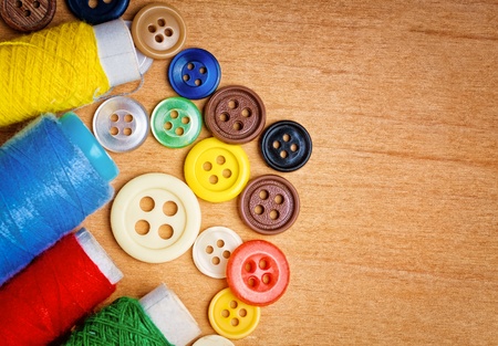 Colorful sewing buttons and thread reels on a wooden background with space for text