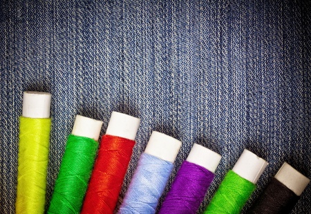 Grunge set of colorful  thread reels creating a frame   on a blue denim fabric with space for textの写真素材