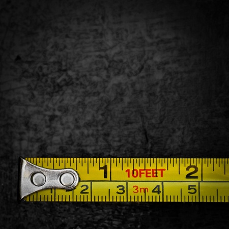 Yellow measuring tape on a textured black metallic background with space for text