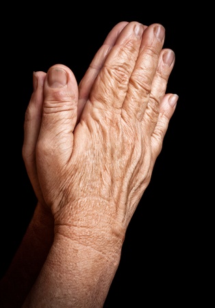 Old wrinkled hands praying isolated on a black backgroundの写真素材