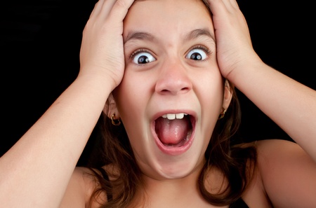 Portrait of a very surprised or scared girl screaming loudly with her hands on her head isolated on a black backgroundの写真素材