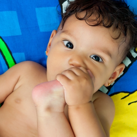 Beautiful mixed race baby girl lying in bed and sucking her toeの写真素材