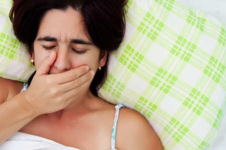 Hispanic woman laying in bed and covering her mouth to avoid coughing or womitingの写真素材