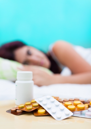Vertical image of an out of focus woman resting in bed with some pills from her medical treatment on a table in the foregroundの写真素材