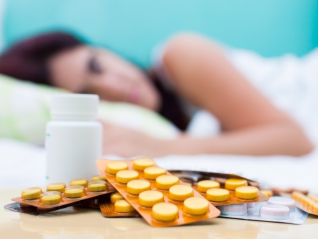 Out of focus woman resting in bed with some pills from her medical treatment on a table in the foregroundの写真素材