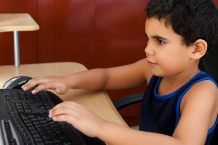Hispanic boy typing on a computer on his bedroomの写真素材
