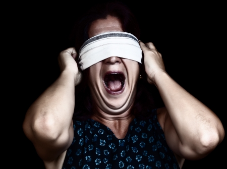 Dramatic image of a frightened woman screaming   and covering her eyes to avoid seeing isolated on black  useful to illustrate crime, gender violence or discrimination の写真素材