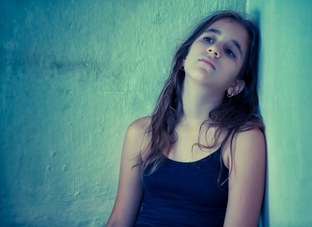 Artistic portrait of a sad hispanic girl sitting next to a dirty wall toned in blue shadesの写真素材
