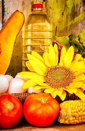 Fresh  vegetables, eggs, flowers and a bottle of oil on a basket with a vintage wooden background useful to illustrate healthy or vegetarian foodの写真素材