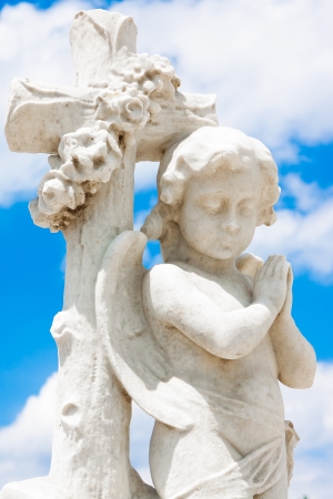 Beautiful infant angel leaning on a christian cross with a blue sky background (with space for text)の写真素材