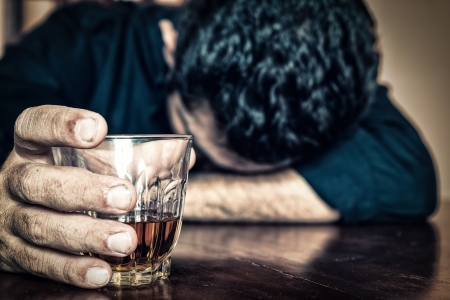 Depressed drunk man holding a drink and sleeping with his head on the table Focused on the drink, his face is out of focus Depressed drunk man holding a drink and sleeping with his head on the table Focused on the drink, his face is out of focus