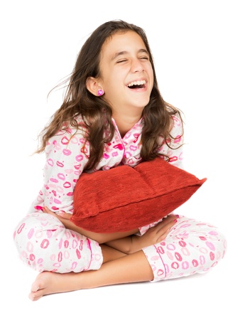 Hispanic teenager wearing pajamas laughing and hugging a red pillow  isolated on white の写真素材