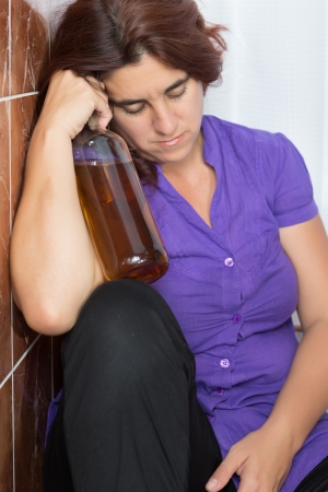 Drunk latin woman sleeping in the bathroom and holding a bottle of liquorの写真素材