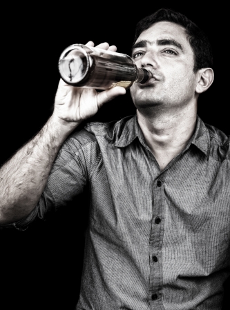 Grunge portrait of a drunk man drinking from a liquor bottle  isolated on black の写真素材