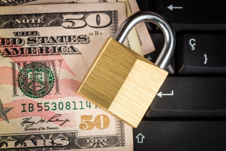 Closed padlock over a stack of money on a black computer keyboard - useful to illustrate financial data securityの写真素材