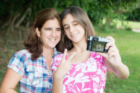 Hispanic teenager and her young mother taking a self picture at a beautiful parkの写真素材