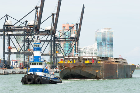 Tugboat pulling a barge in the Port of Miami with containers and cranes on the backgroundのeditorial素材