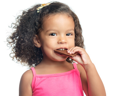 Joyful little girl with an afro hairstyle eating a chocolate bar isolated on whiteの写真素材