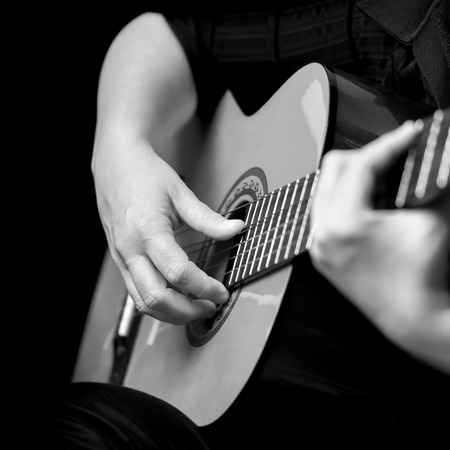 Acoustic guitar detail on black and white - Musician hands playing a classic guitar isolated on a black backgroundの写真素材