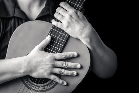 Acoustic guitar detail on black and white - Musician hands playing a classic guitar isolated on a...