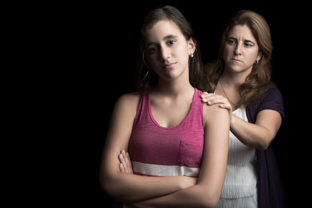 Sad and troubled teenage girl with her mother trying to comfort her isolated on black