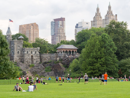 People enjoying a day at Central Park with a view of Belvedere Castle and nearby historic buildings in New Yorkのeditorial素材