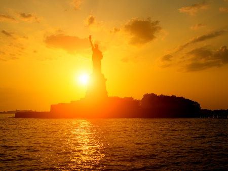 The Statue of Liberty at sunset with the sun shining on the oceanの写真素材