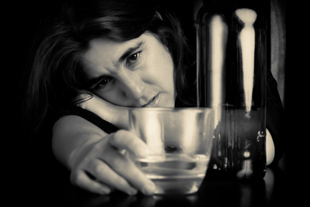 Drunk and depressed lonely woman holding a glass of whisky with a sad expressionの写真素材