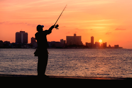 Beautiful sunset in Havana with the silhouette of a fisherman on the Malecon seawallの写真素材