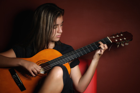 Beautiful teenage girl playing an acoustic guitar photographed in a low key style