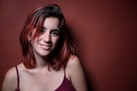 Portrait of a beautiful red haired teenage girl photographed on a matching red backgroundの写真素材