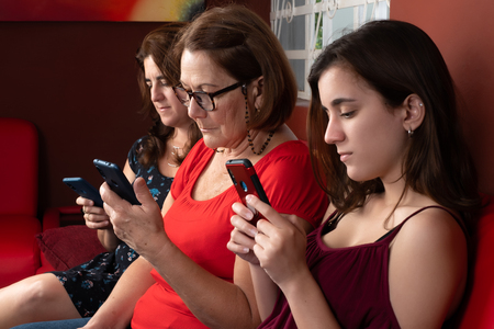 Three generations of hispanic women looking at their smartphones at home