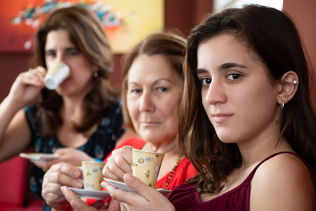Three generations of hispanic women drinking coffee at homeの写真素材