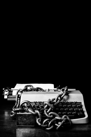 Information censorship concept - Typewriter locked with a chain and padlock - In black and white isolated on a black backgroundの写真素材