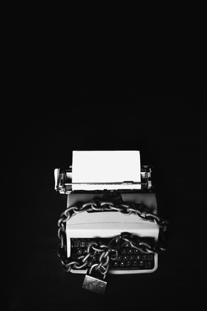 Information censorship concept - Typewriter locked with a chain and padlock on a black backgroundの写真素材